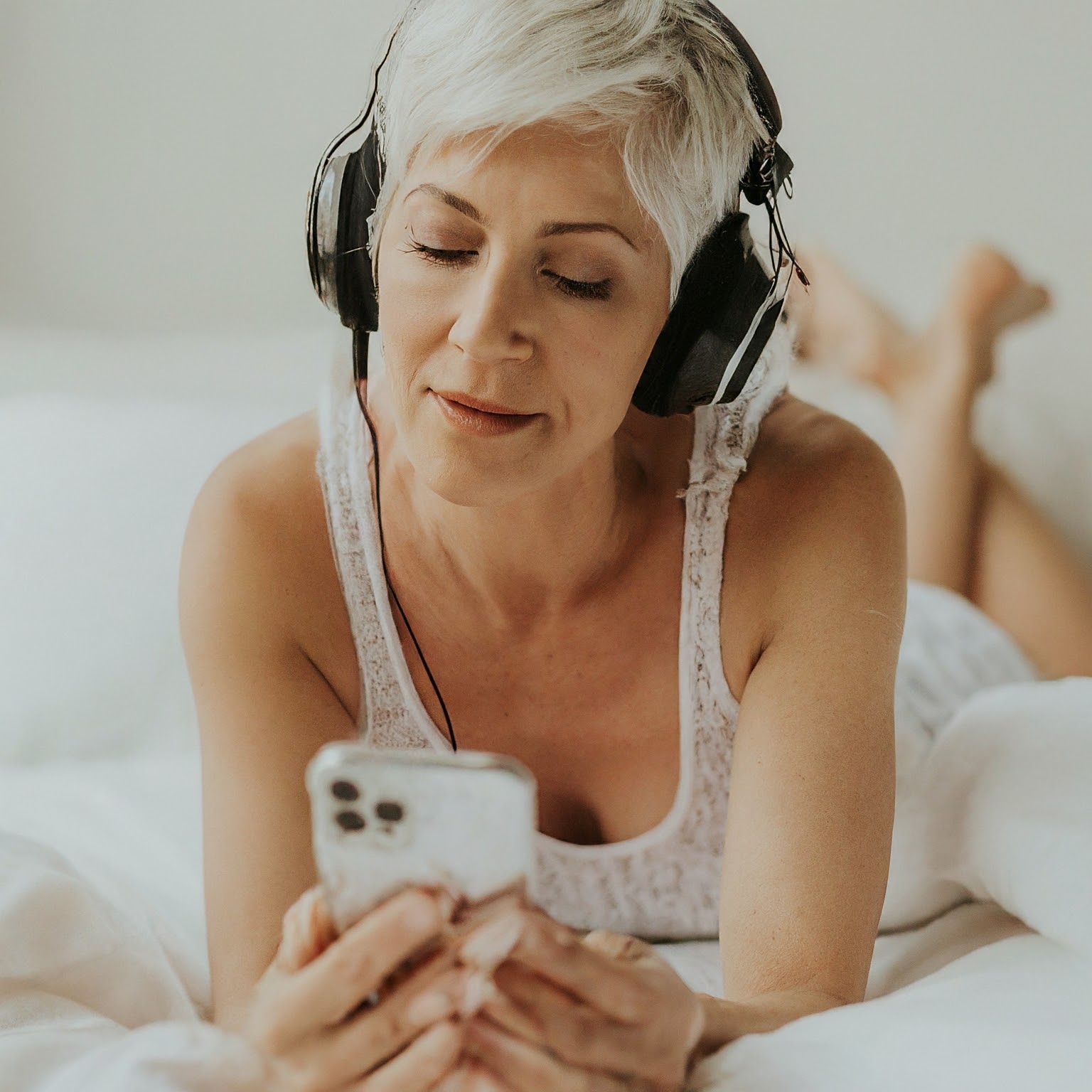 Woman wearing headphones while lying in bed and listening to deep sleep music on her phone.