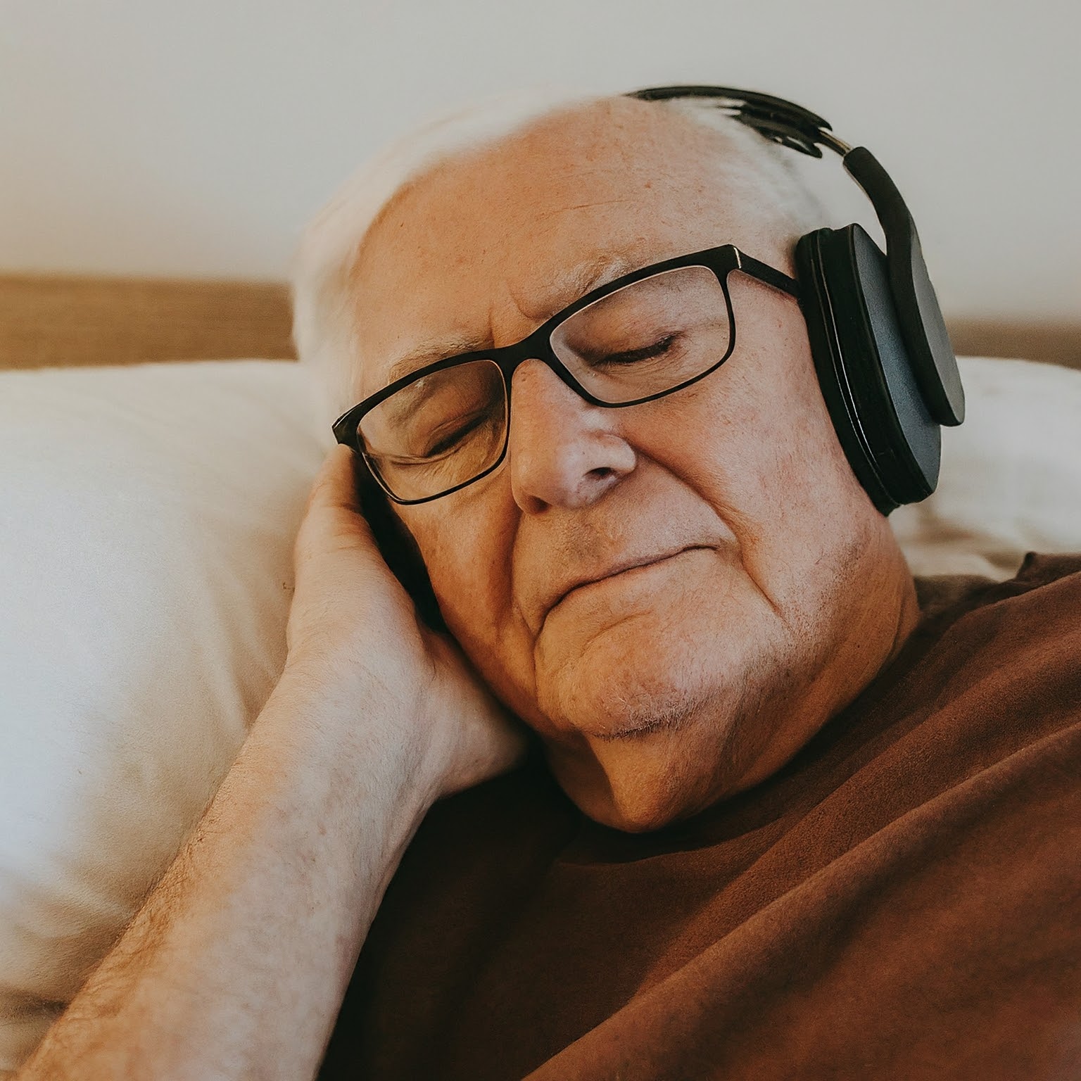 Older man resting in bed while listening to pink noise through headphones.