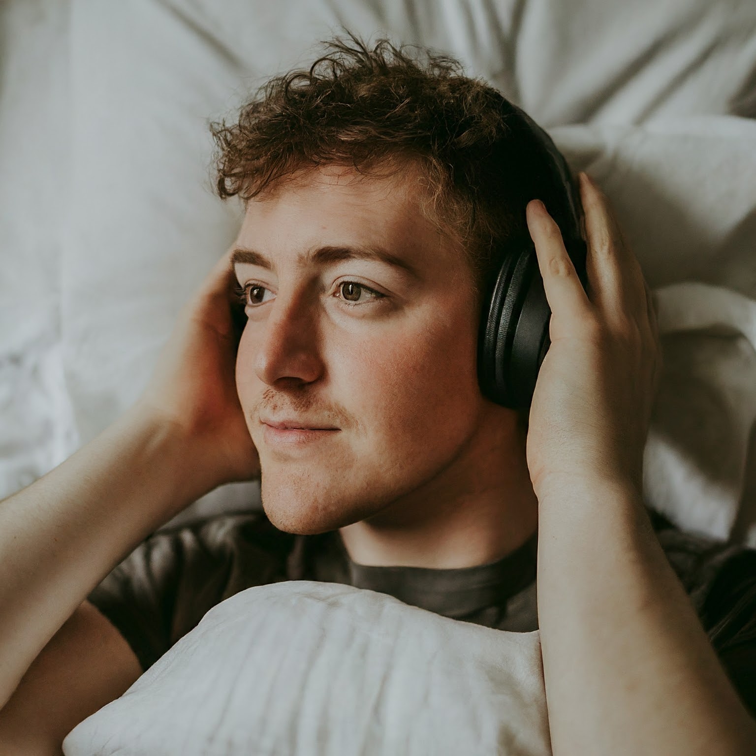Man lying in bed wearing headphones while listening to sleep music for deep sleeping.
