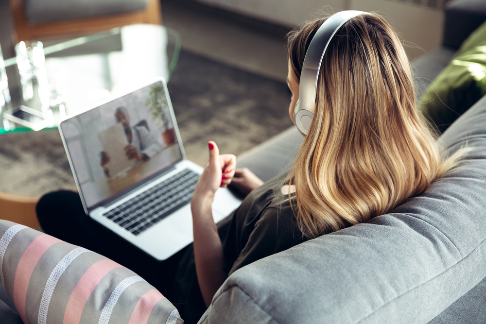 Woman wearing headphones attends an online coaching session on a laptop from home while sitting on a couch.