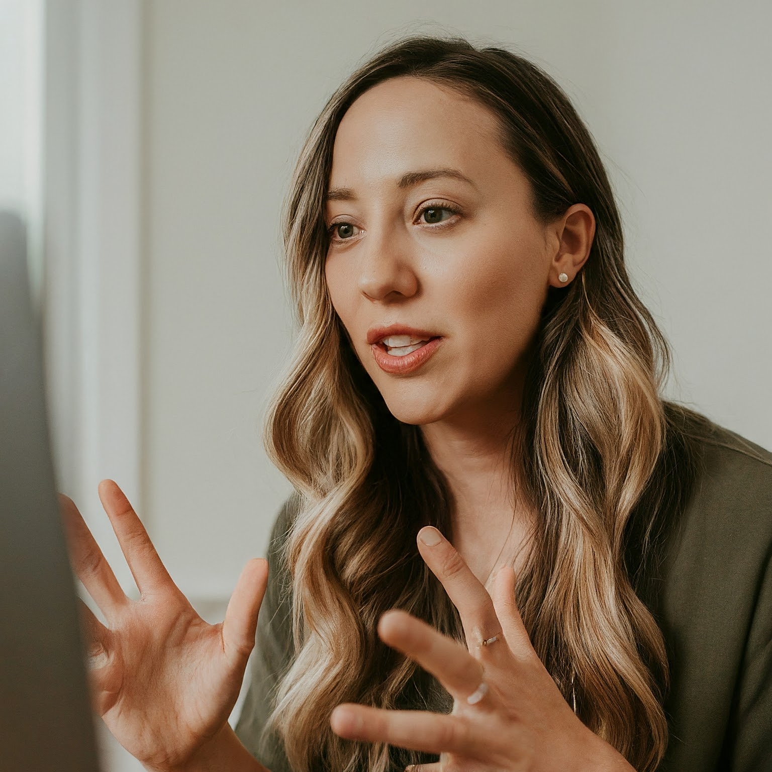 Online sleep coach speaking during a virtual consultation, gesturing toward a computer screen in a bright home office setting.