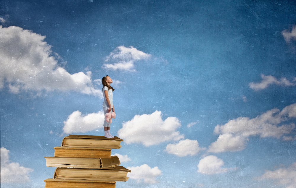 Young girl holding stuffed animals stands on a stack of books against a blue sky with clouds, symbolizing dreams, learning, imagination, and childhood growth.