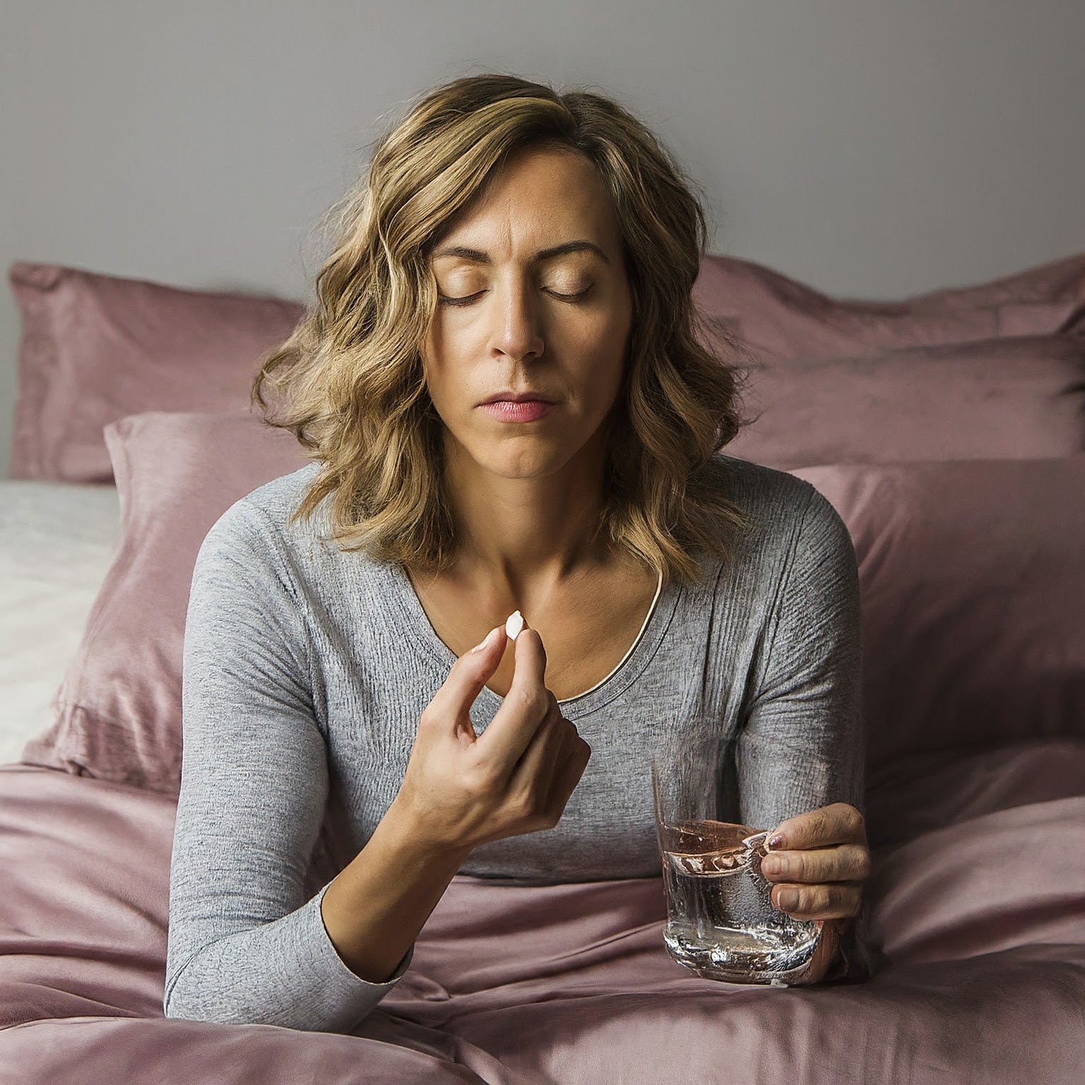 Woman sitting in bed holding a sleeping pill and glass of water, representing sleep medication and insomnia treatment.