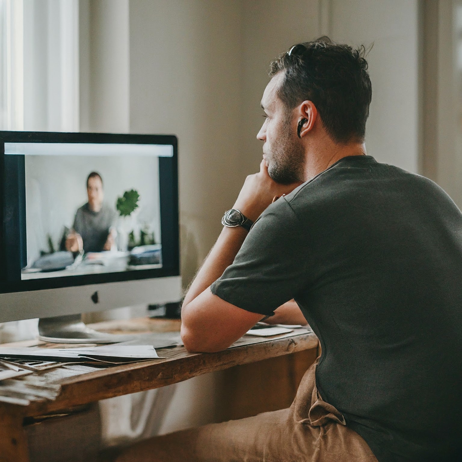 Man wearing an earbud during an online sleep coaching session with a specialist on a desktop computer at home.