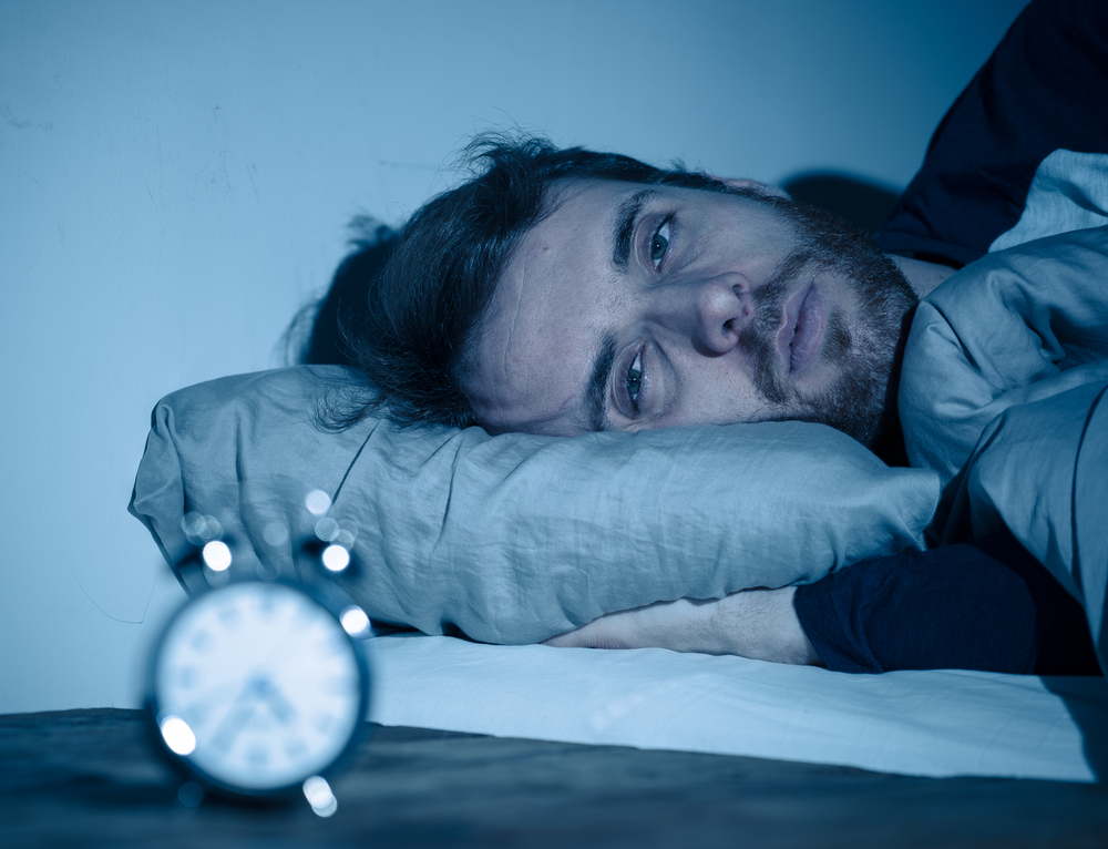 Man lying awake in bed at night with an alarm clock nearby, suggesting insomnia or trouble sleeping.